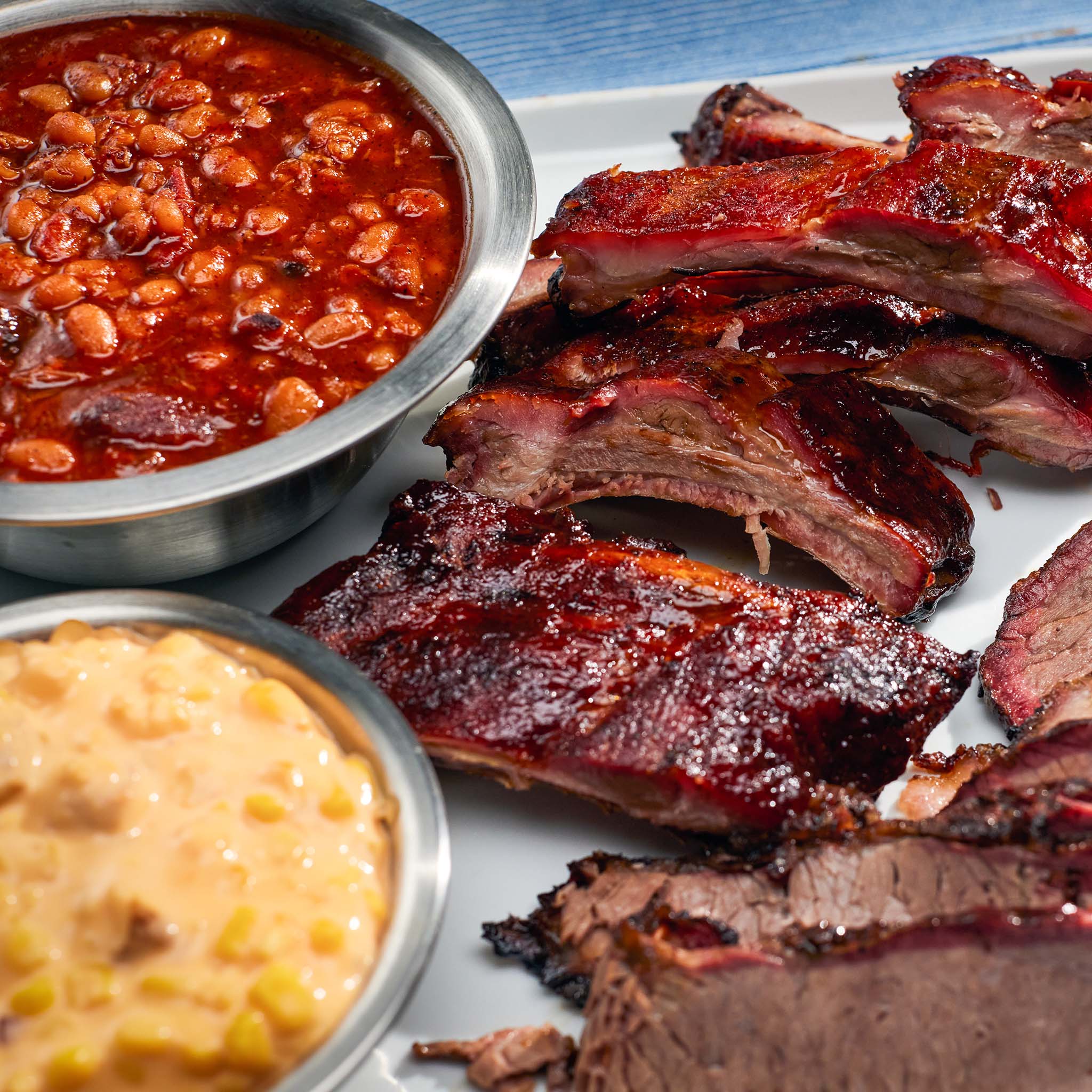Platter of barbecue ribs with a side of baked beans and cornbread.