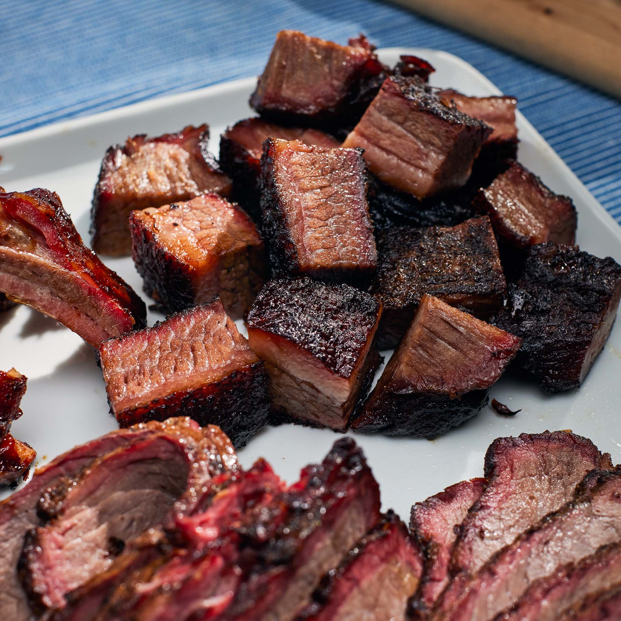 Close-up of smoked meat cubes on a white plate with a blue cloth background