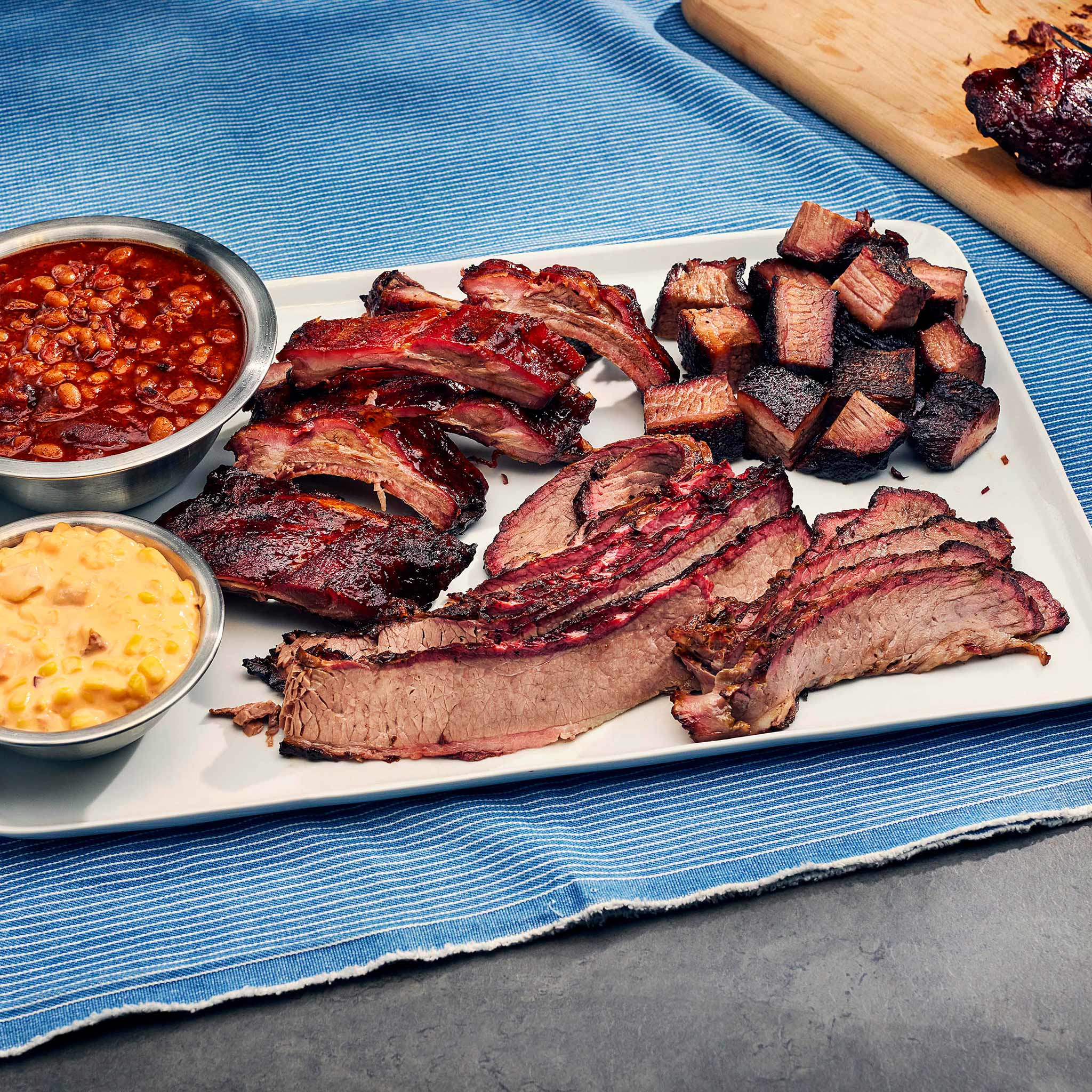 Platter of barbecue meats with sides on a blue tablecloth