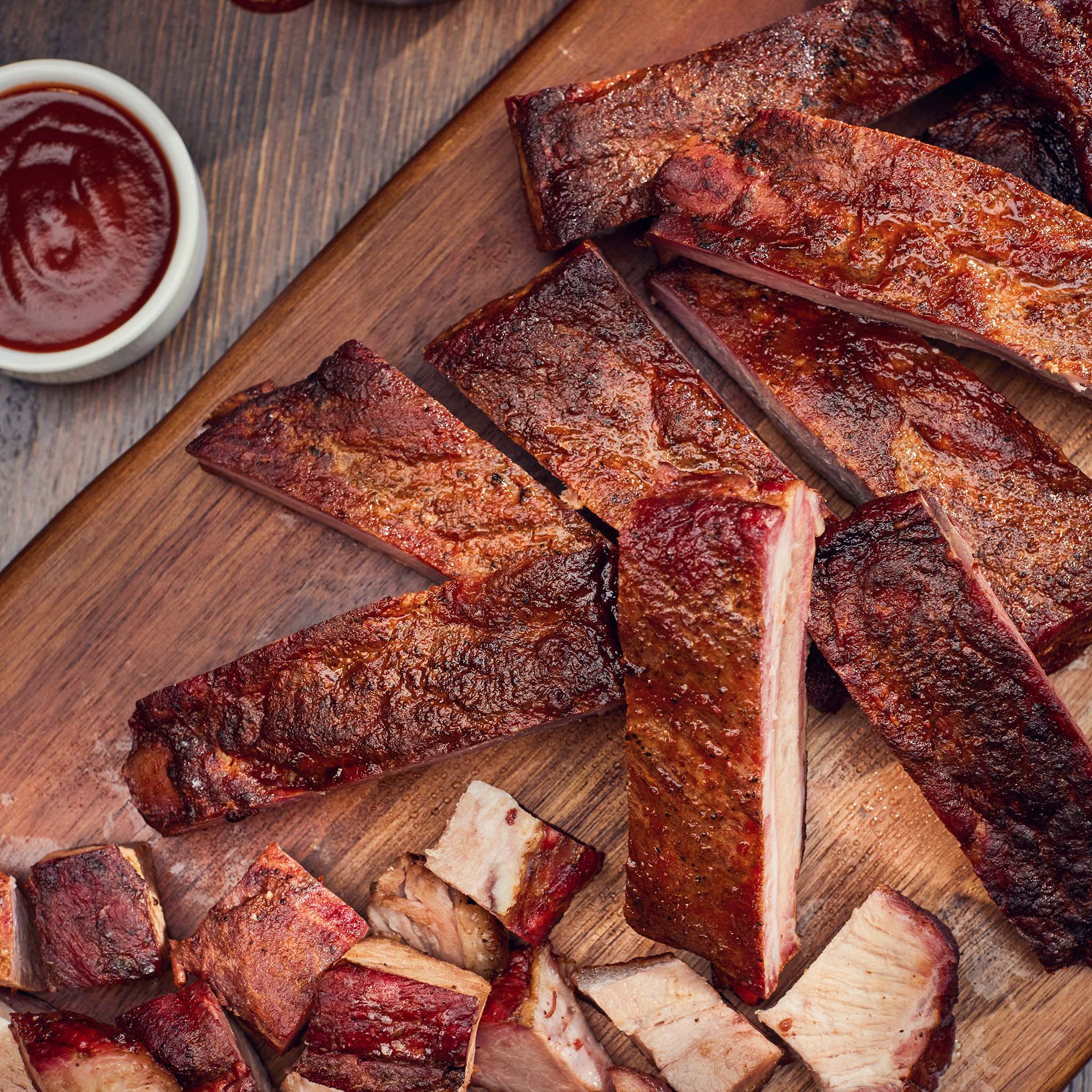 Sliced ribs on a wooden cutting board with a side of barbecue sauce.