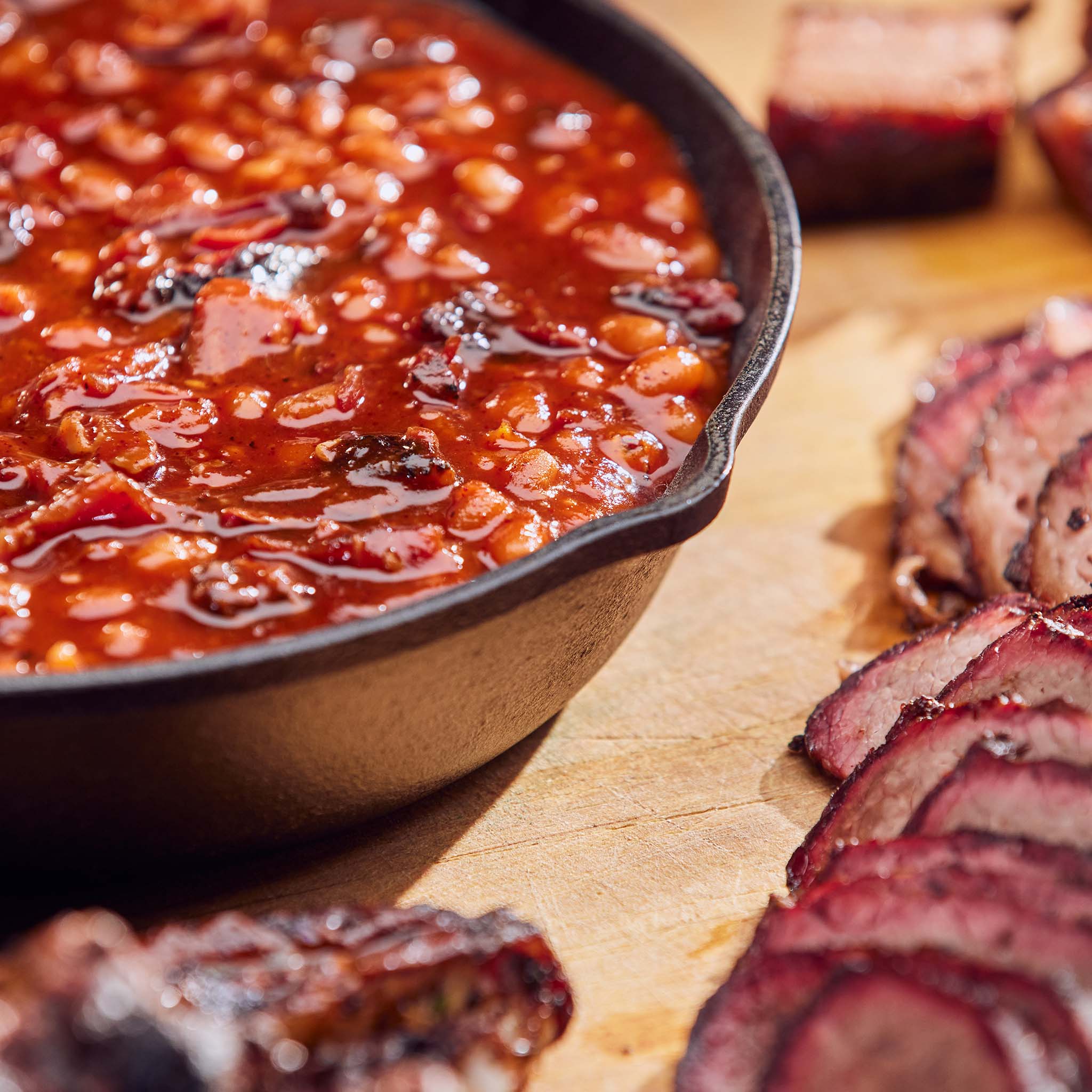 Baked beans in a skillet with sliced sausages on a wooden surface