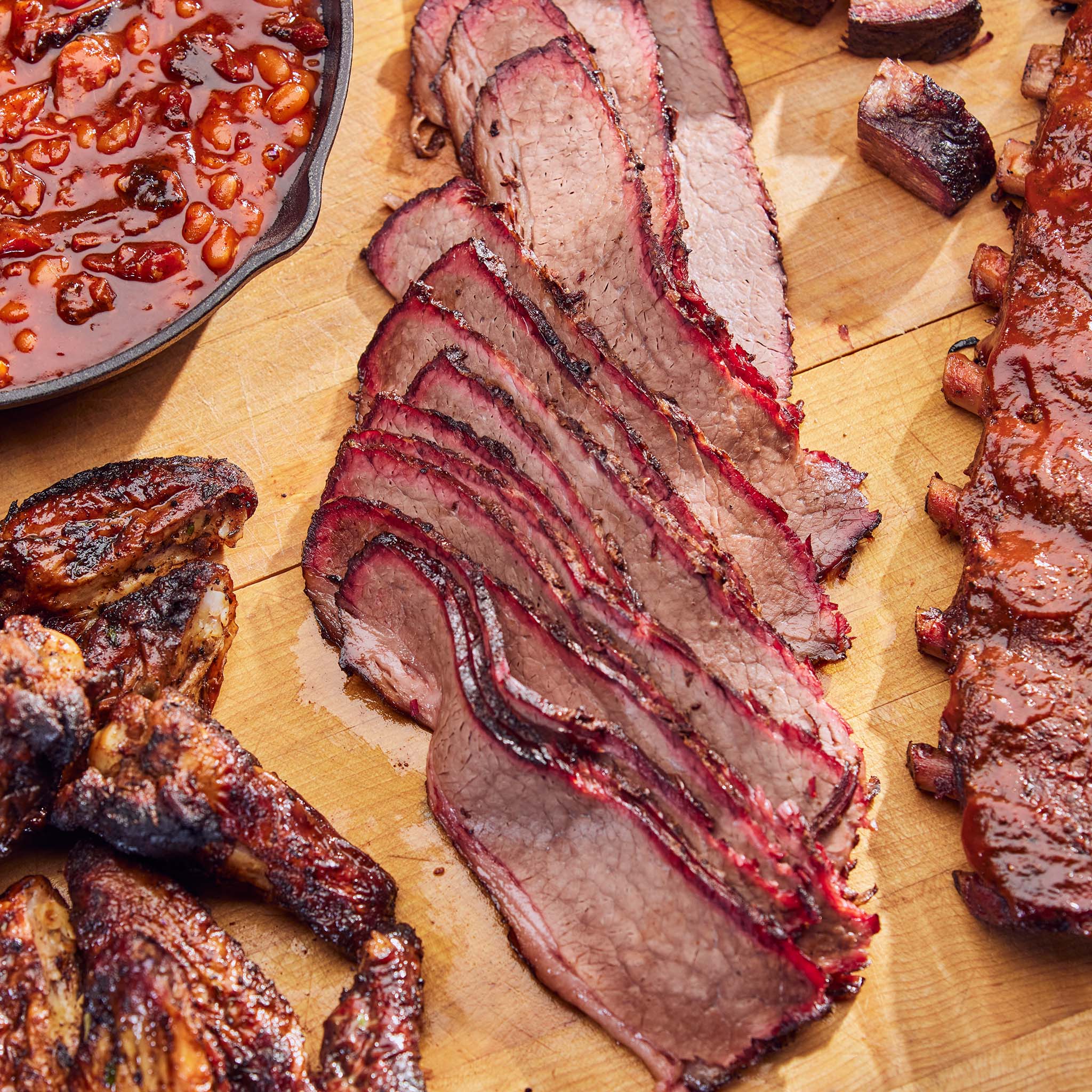 Sliced brisket on a wooden cutting board with beans and other meats.