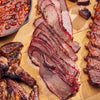 Sliced brisket on a wooden cutting board with beans and other meats.