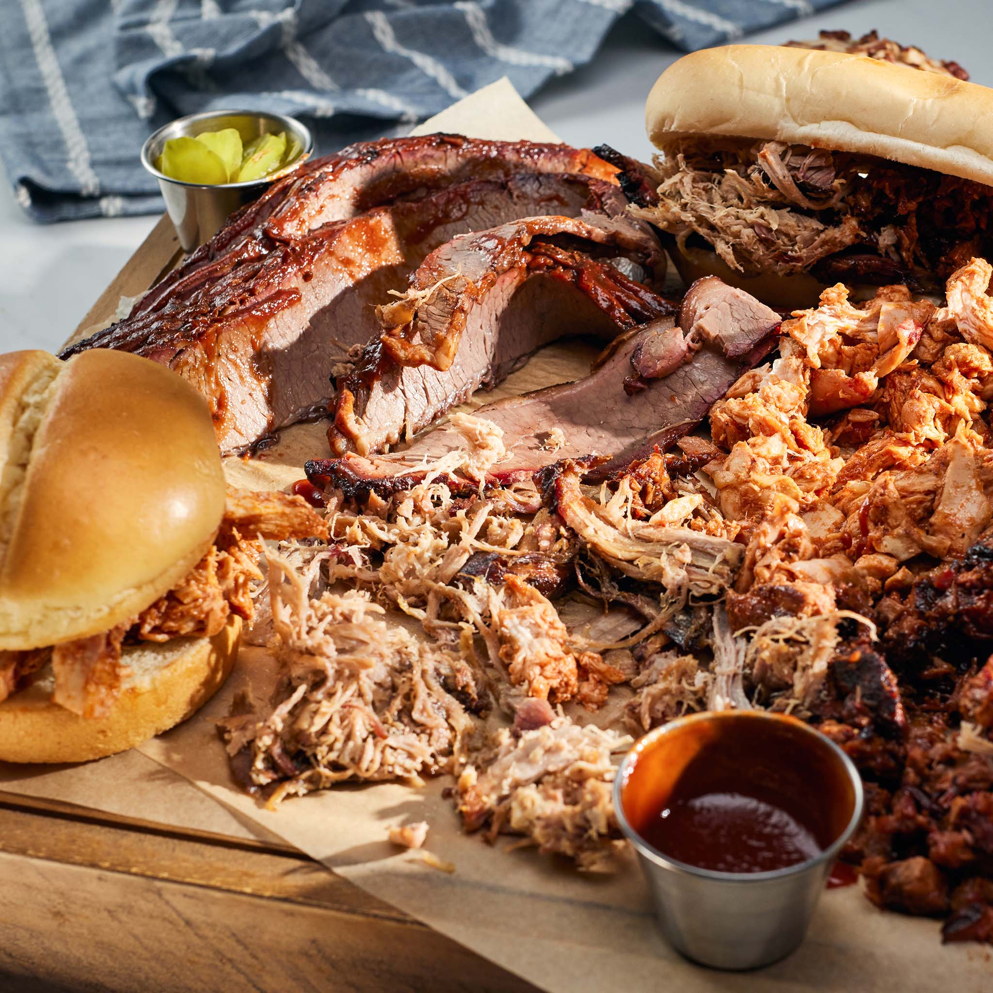 Platter of pulled pork sandwiches and sides on a wooden board with a blue towel in the background.