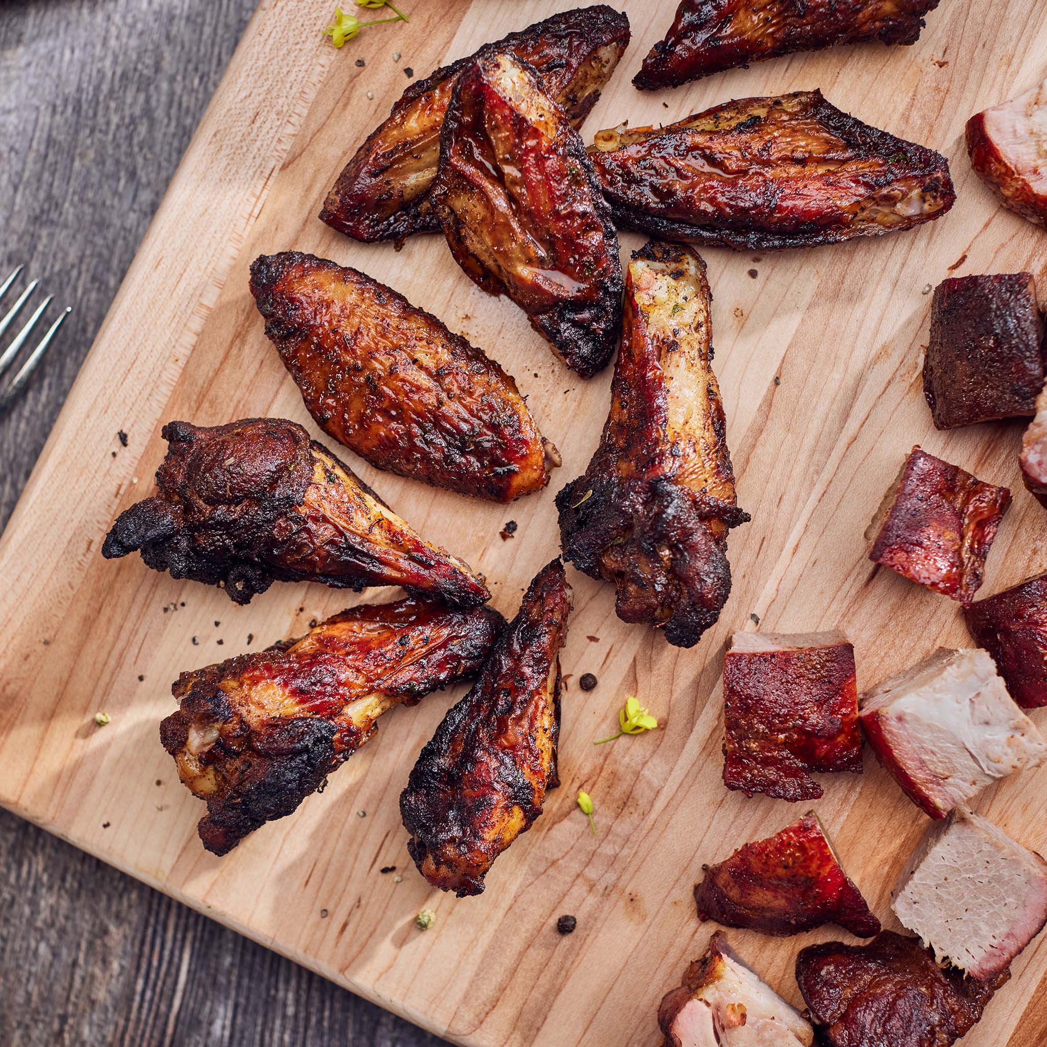 Grilled chicken wings and pieces on a wooden cutting board.
