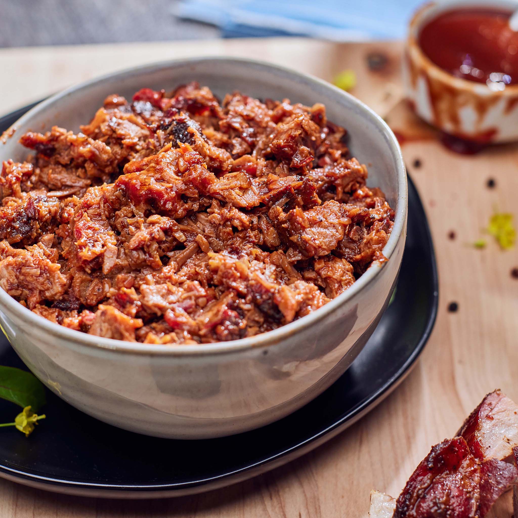 Bowl of shredded beef on a wooden table with a small bowl of sauce in the background.