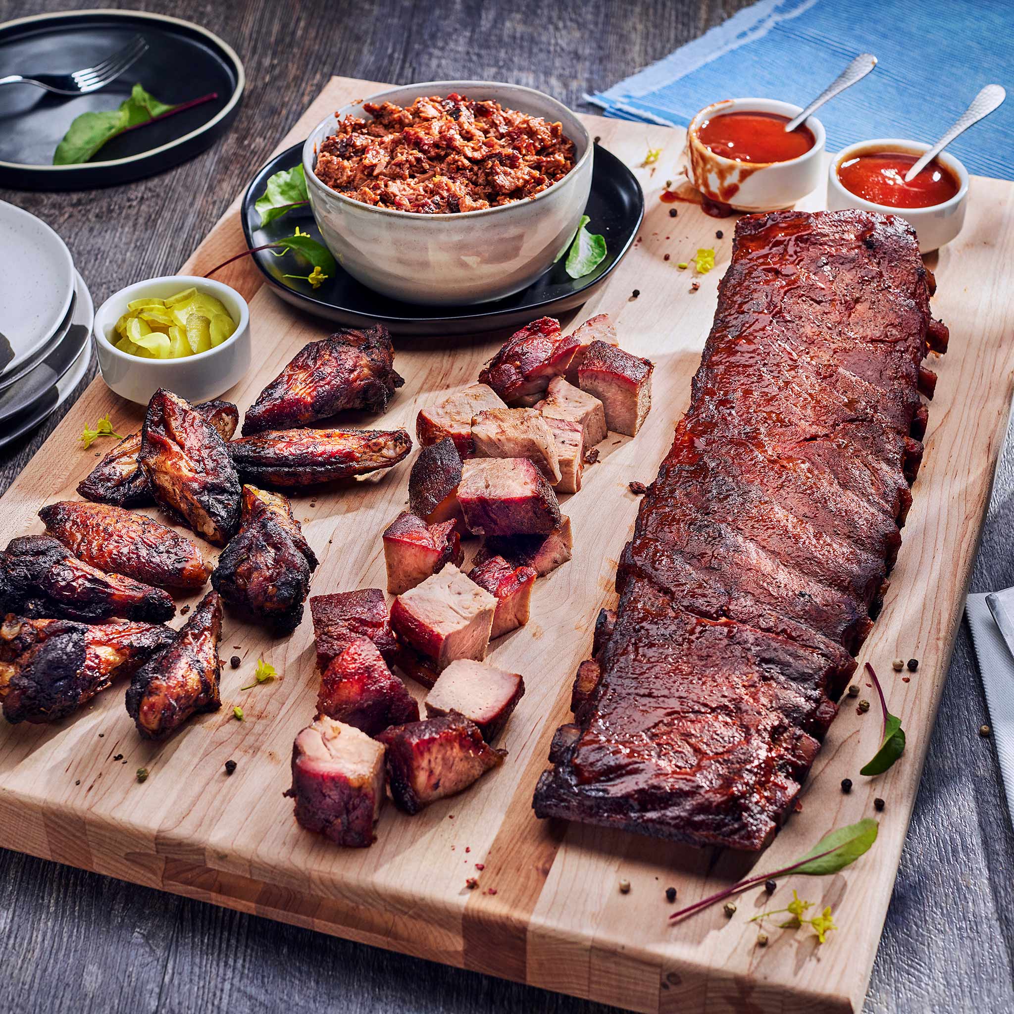Assorted barbecue meats on a wooden cutting board with side dishes.