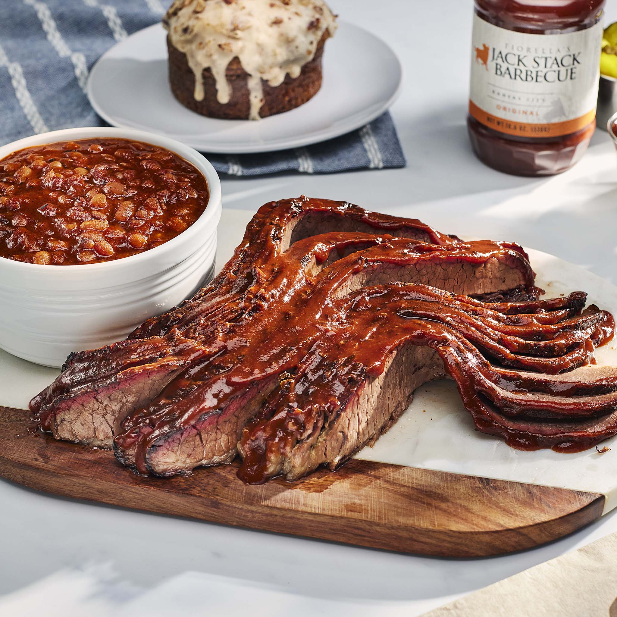Barbecued ribs on a wooden cutting board with baked beans and a dessert in the background.