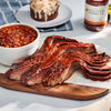 Barbecued ribs on a wooden cutting board with baked beans and a dessert in the background.
