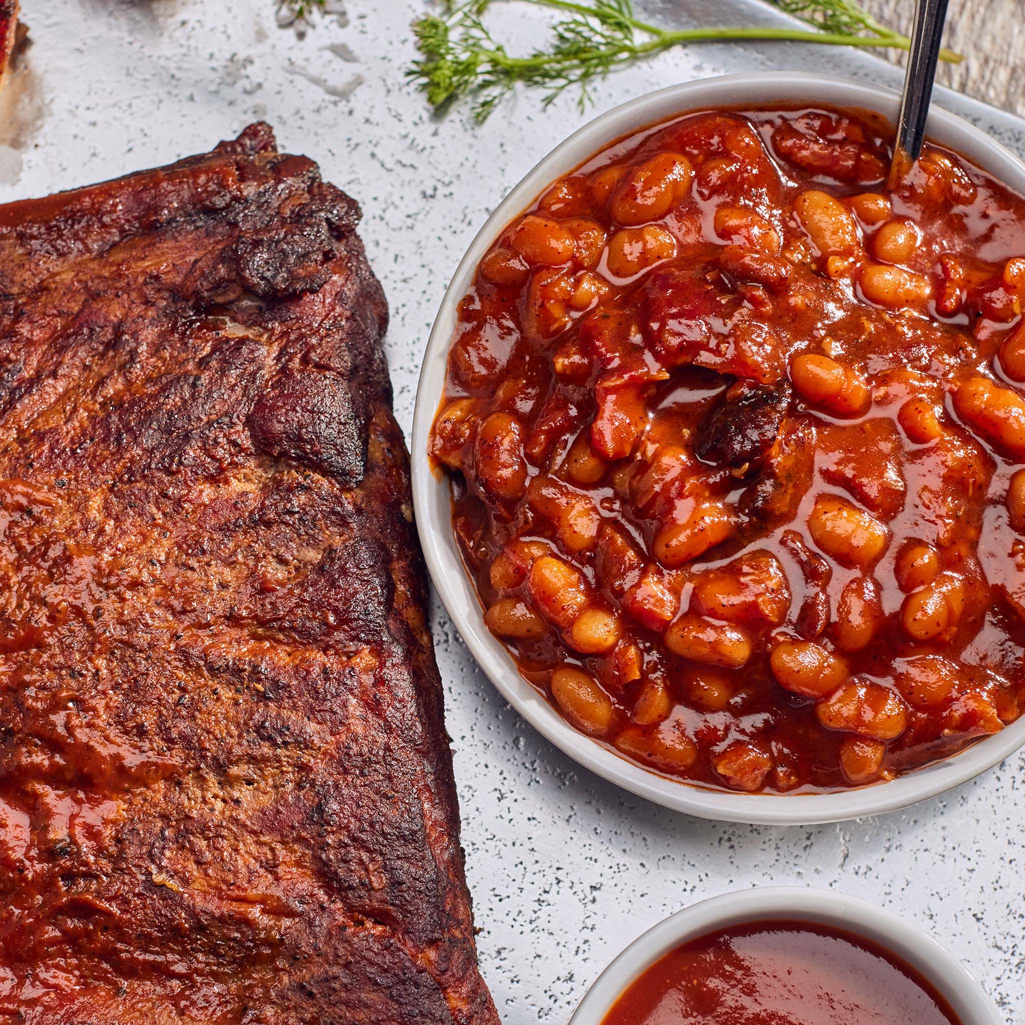 Barbecue ribs and baked beans on a white surface with a spoon.