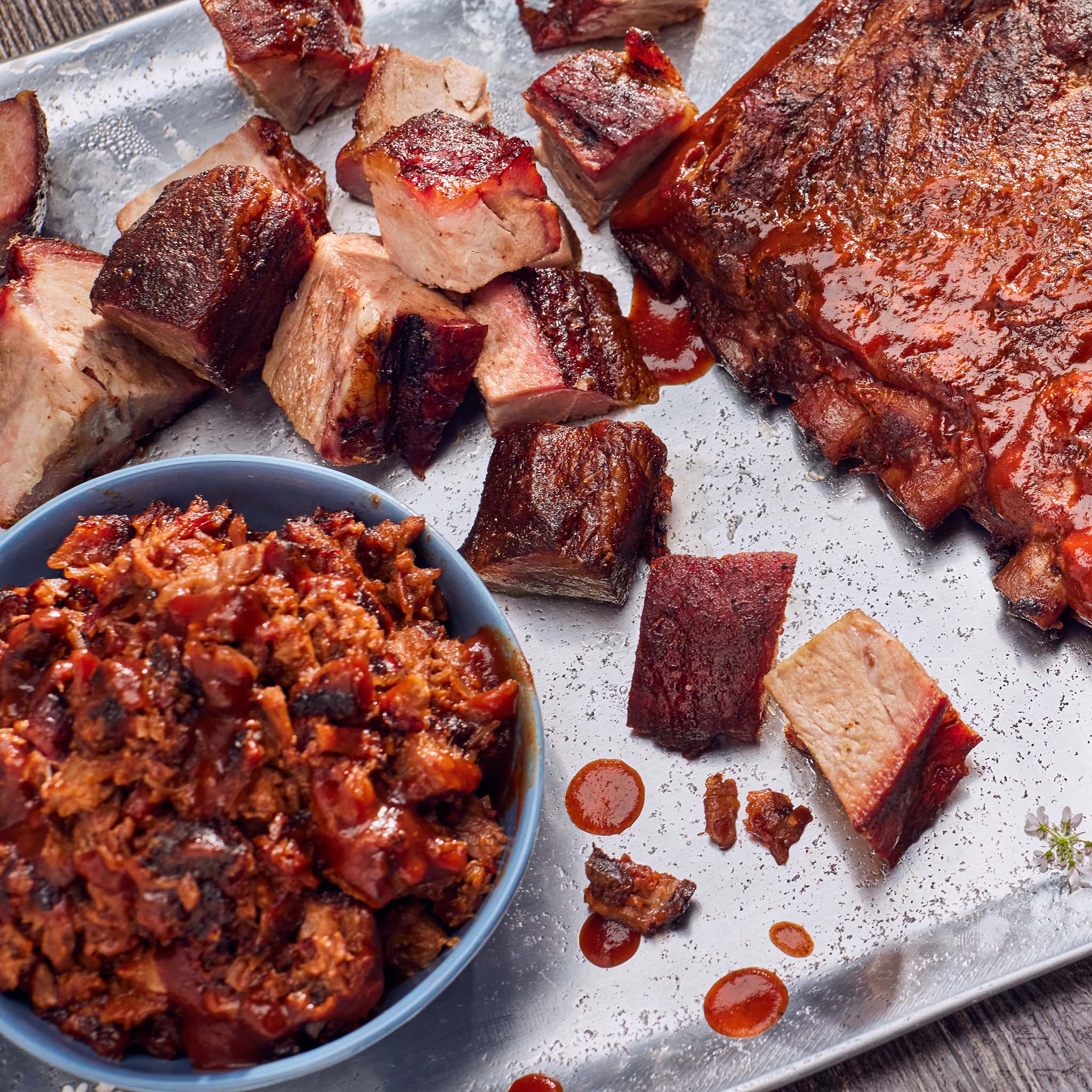 Meat dish with chunks of cooked meat and a bowl of meat-based spread on a metal tray.