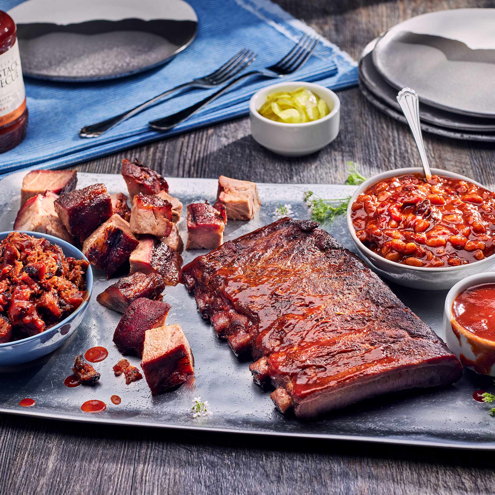 Plated barbecue meal with ribs, pulled pork, and sides on a wooden table.