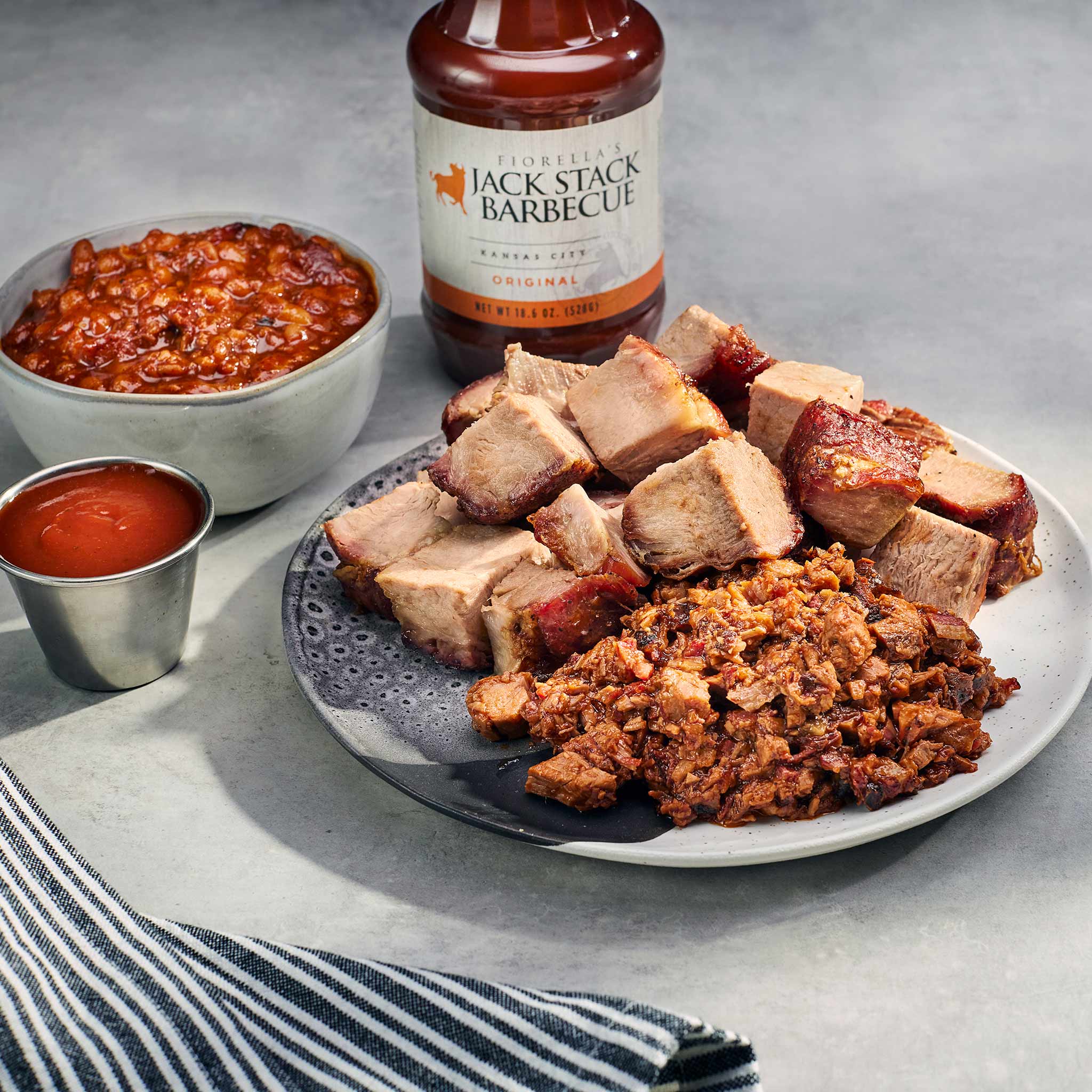 Plated barbecue meal with Jack Stack Barbecue sauce, beans, and pulled pork on a gray surface.