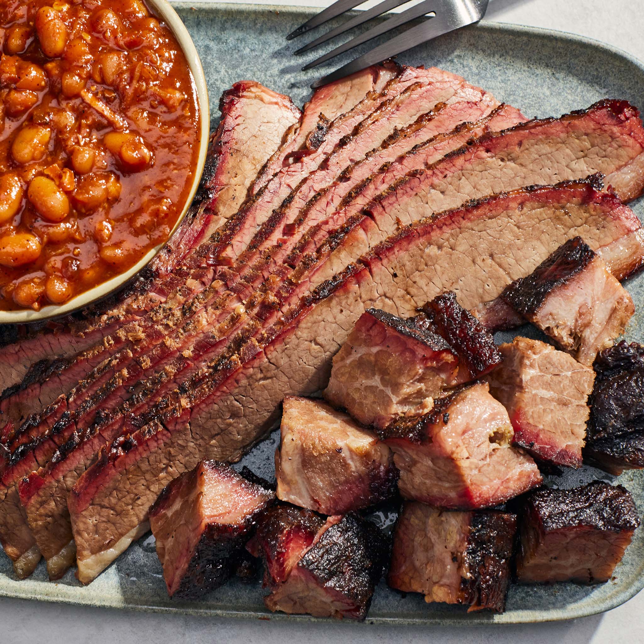 Plated barbecue brisket with a side of baked beans on a gray plate.