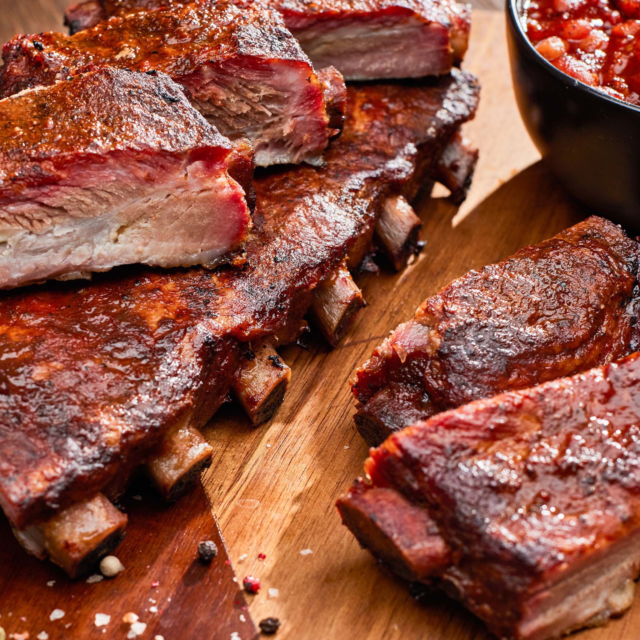 Barbecue ribs on a wooden cutting board with a side of sauce.