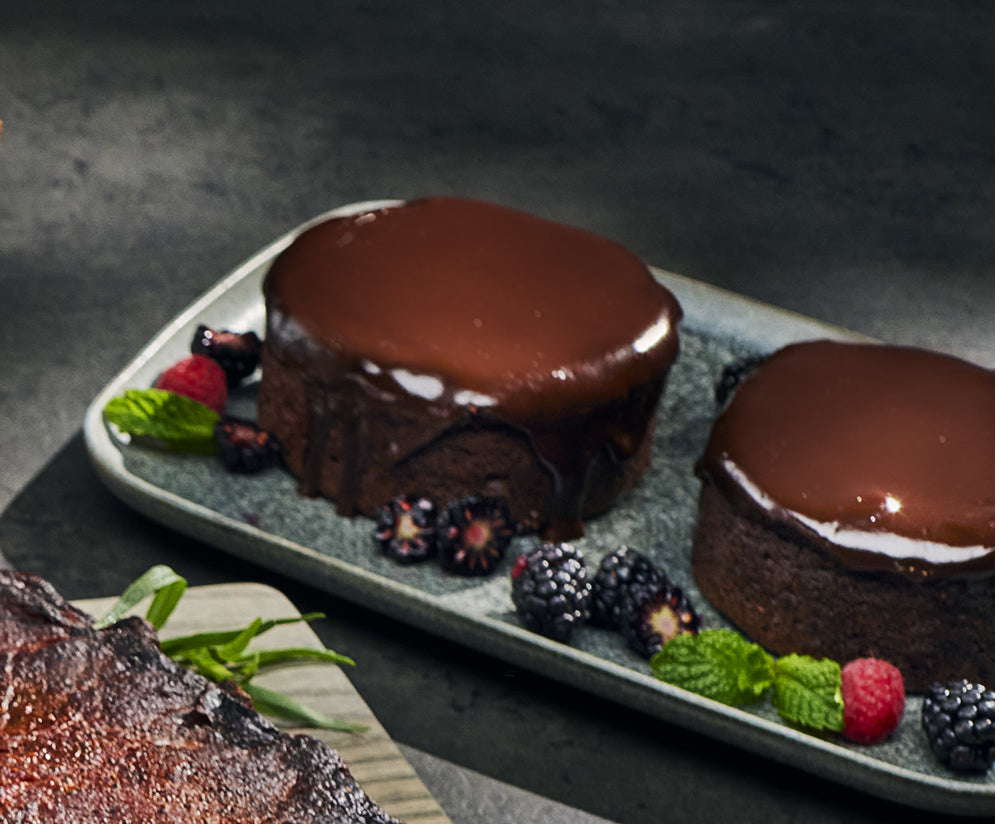 Two chocolate desserts on a plate with berries and mint leaves on a dark background