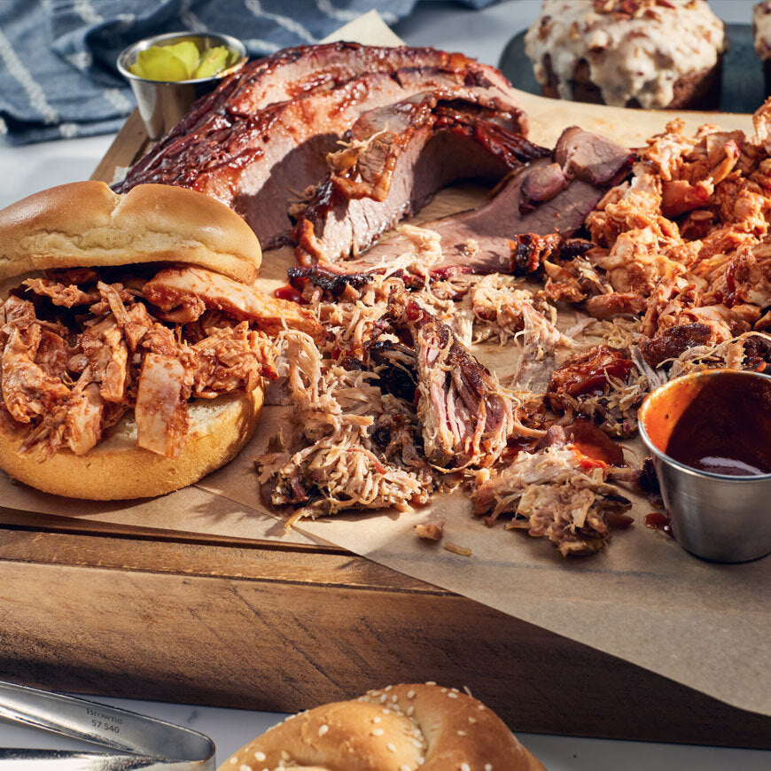 Pulled pork on buns and a wooden cutting board with additional pulled pork and condiments.