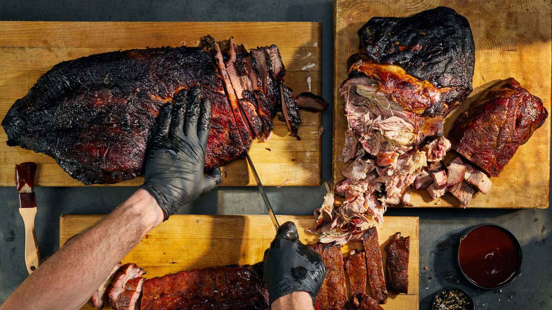 Person cutting smoked meat on a wooden cutting board with a knife.