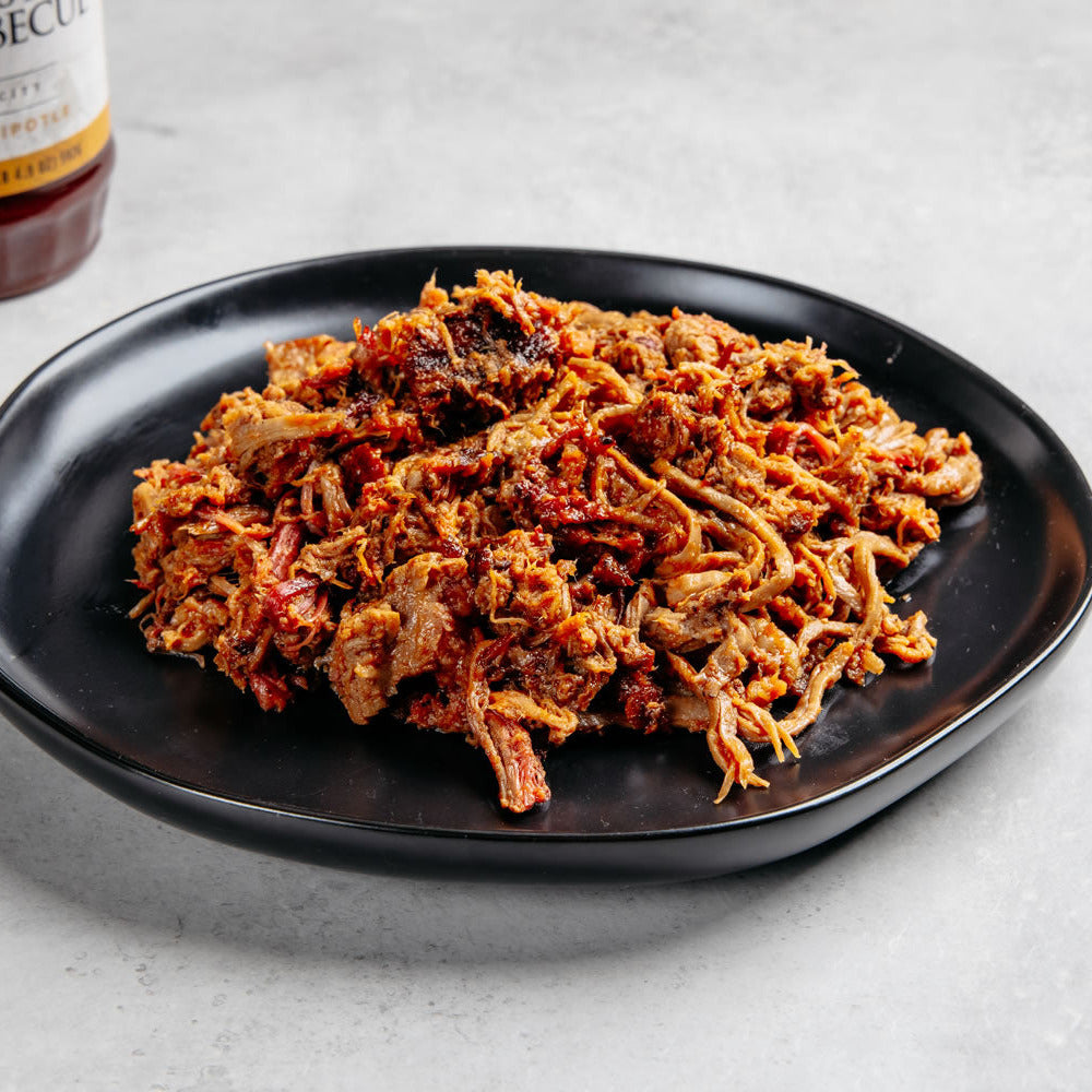 Plated barbecue  brisket with a bottle of barbecue sauce on a light gray background